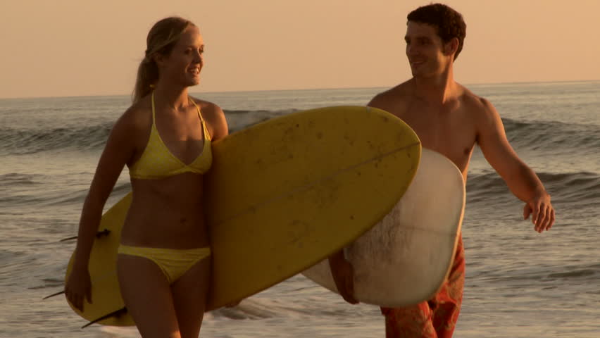 Young couple walking with surfboards on beach at sunset