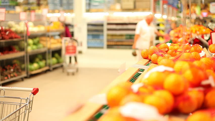 Mother and son approaching the orange shelf, choosing some oranges and putting them into the trolley 