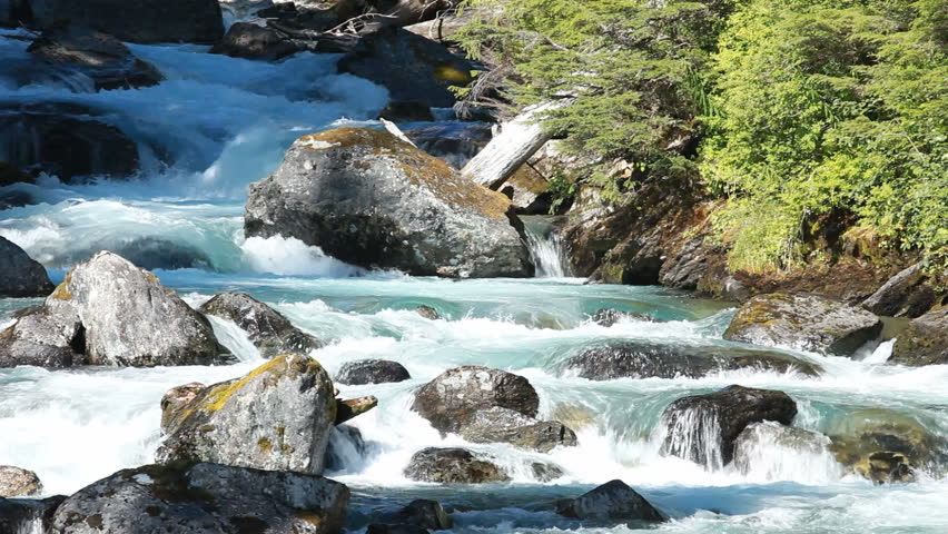 Waterfall through rough broken smooth rocks high in the mountains of Alaska. Forest and vegetation along edge of water. Blue glacial snow and ice melt. Relaxing and calming.