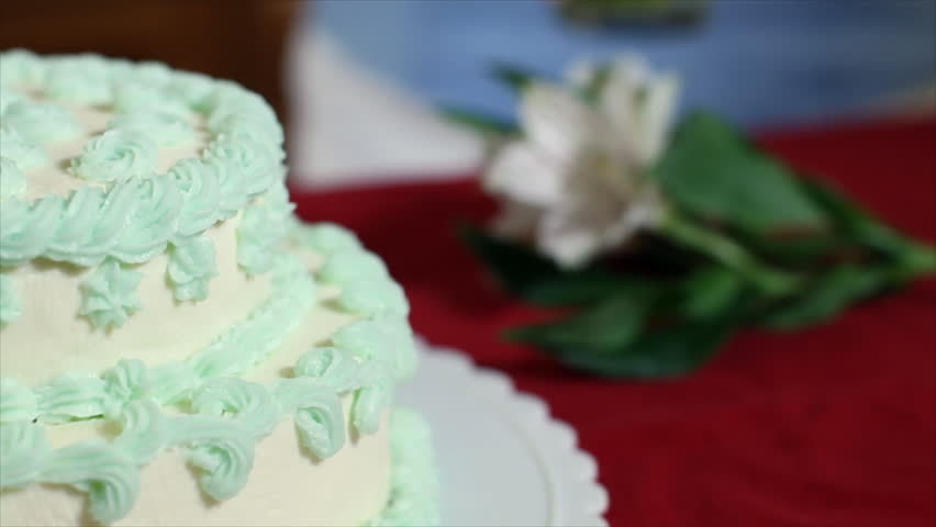 The camera pans across a lovely tiered cake with white fondant icing decorated in pale green flowerets and lacy borders.