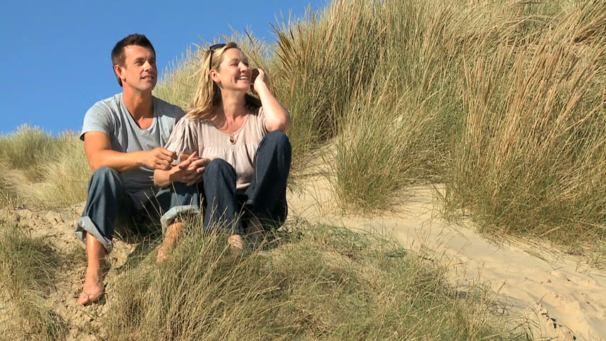 Attractive young caucasian couple enjoying quiet time together sitting in sand dunes at the coast filmed at 60FPS