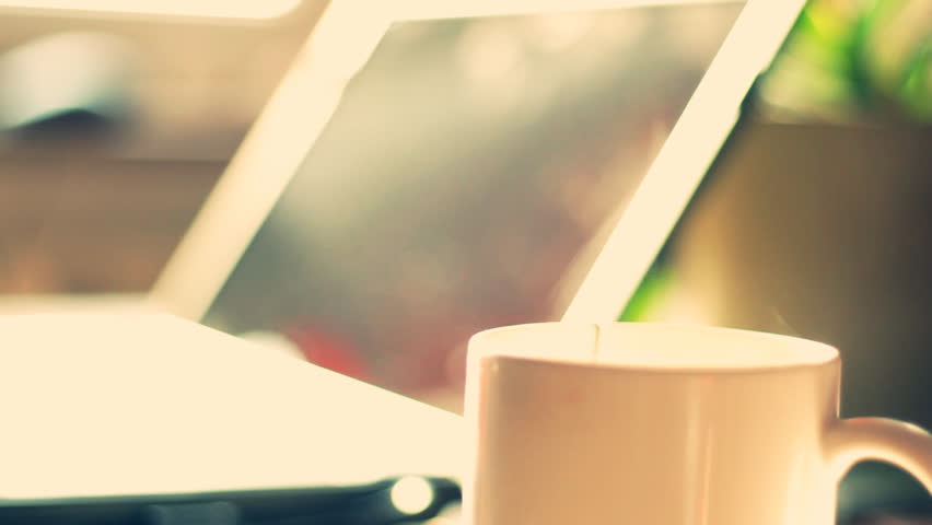 Steamy cup of coffee or tea with laptop in background 