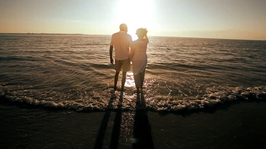 Mature couple in the shallows at the edge of the beach enjoying a tranquil evening at sunset