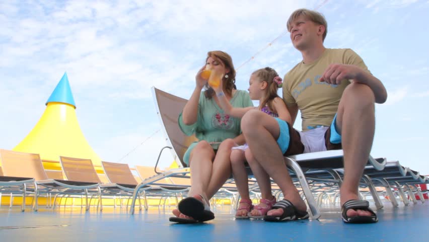 family of three drink juice, sitting on deckchairs on cruise ship