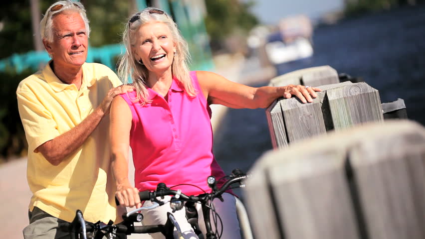 Healthy active senior couple enjoying their retirement leisure cycling by a waterway