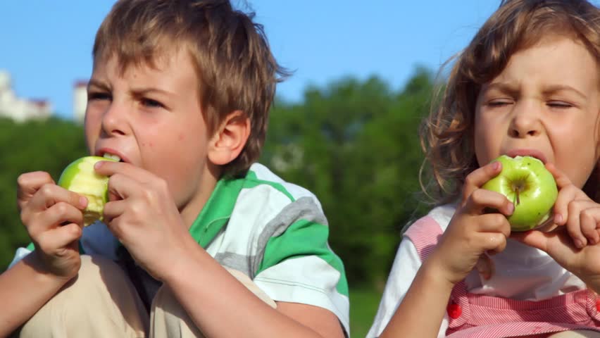 boy with girl sitting and eating green apples outdoor