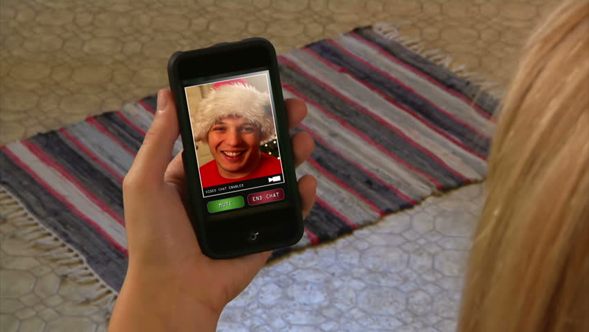Male in Santa hat video chatting on a generic, portable handheld device.  Screen images simulated.
