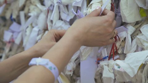 The female hands strongly ties up wish clothes attached on wish wall in Virgin Mary House. 4K
