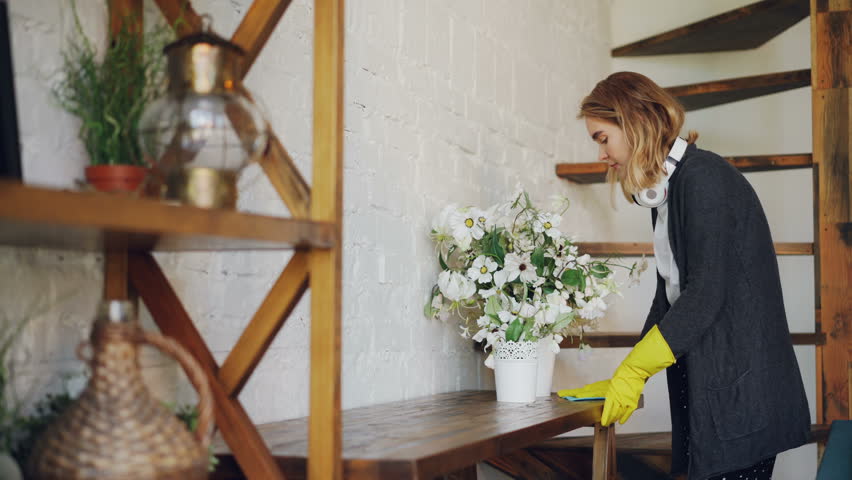 Professional Housekeeper Is Dusting Furniture With Wet Cloth Woman Is Wearing Protective Gloves Casual Clothing And Headphones Professional Housekeeper Is Dusting Furniture With Wet Cloth Woman Is Wearing Protective Gloves Casual Clothing And Headphones