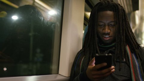 Handsome Black Man With Dreadlocks Checking His Phone On A Train At Night