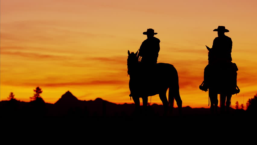 Dusk Shot Of Four Cowboys Riding Off Into The Sunset Towards Mountains ...