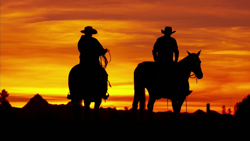 Dusk Shot Of Four Cowboys Riding Off Into The Sunset Towards Mountains ...