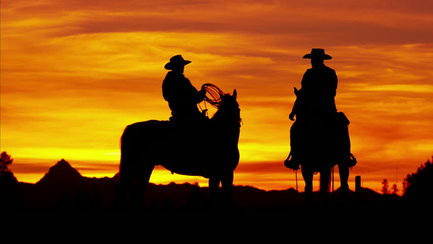 Dusk Shot Of Four Cowboys Riding Off Into The Sunset Towards Mountains ...