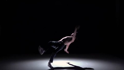 Dancer man with naked and denim torso starts dancing breakdance on black, shadow, slow motion