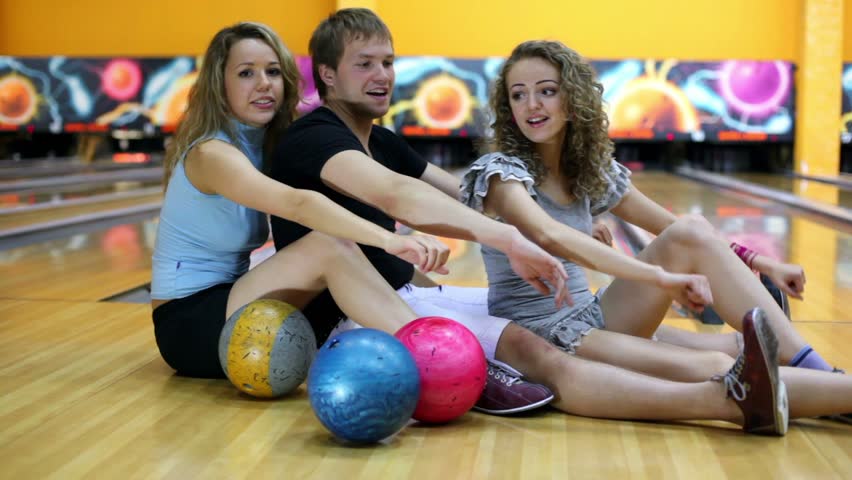 Two Girls Stand Behind Boy And They Dance With Bowling Balls In Club