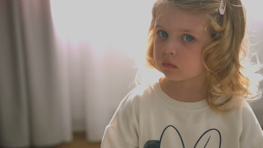 Portrait Of Serious Caucasian Little Girl With Blond Curly Hair And Blue