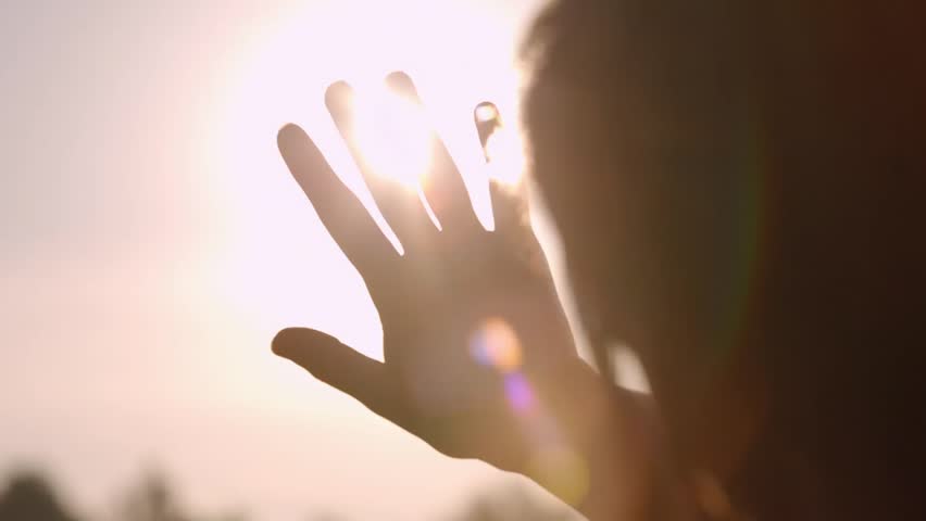 Girl looks at the sun through her hand