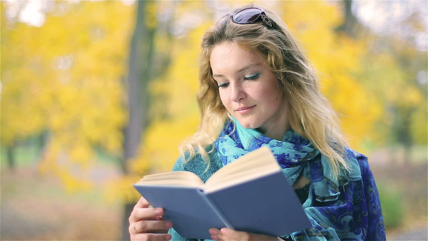Pretty girl with freckles reading book in the park